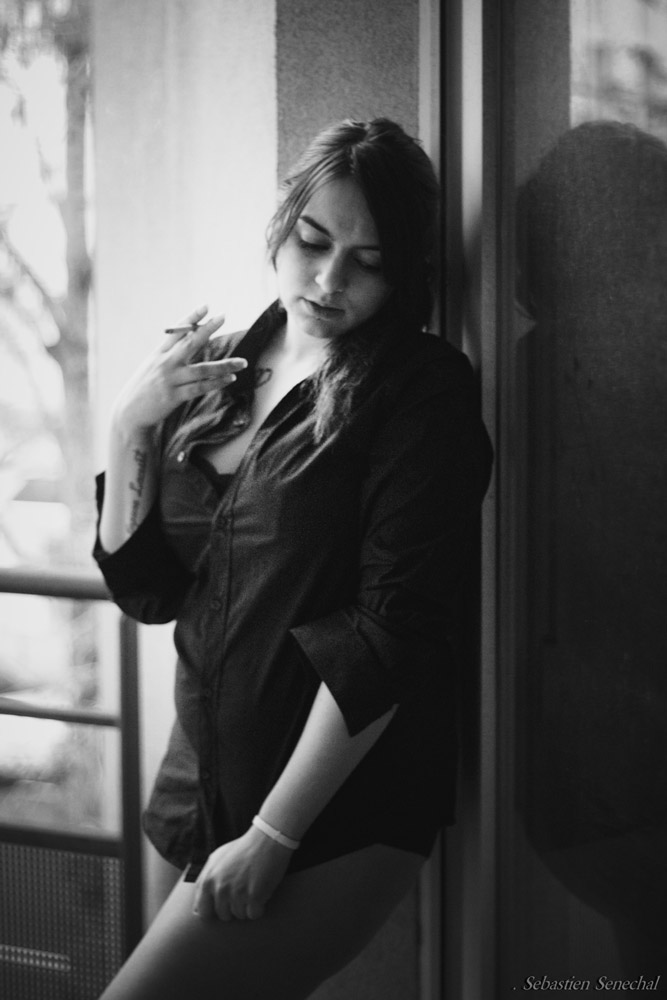 Une jeune femme fume une cigarette sur son balcon en petite tenue.